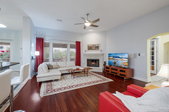 living area featuring ceiling fan, a fireplace, arched walkways, baseboards, and wood finished floors