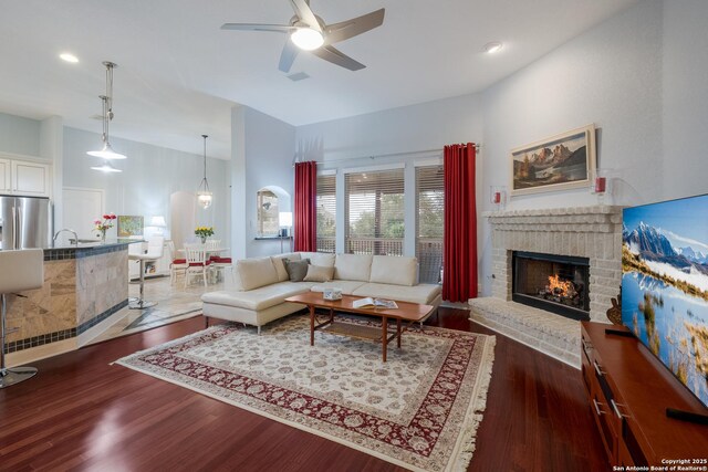 living area featuring a brick fireplace, a ceiling fan, recessed lighting, and dark wood-style flooring