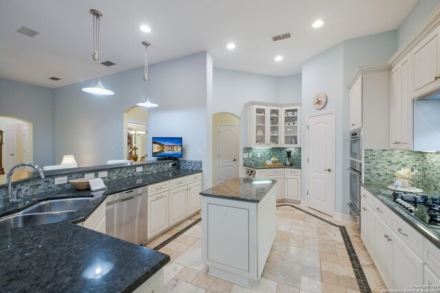 kitchen featuring appliances with stainless steel finishes, a sink, arched walkways, a kitchen island, and visible vents