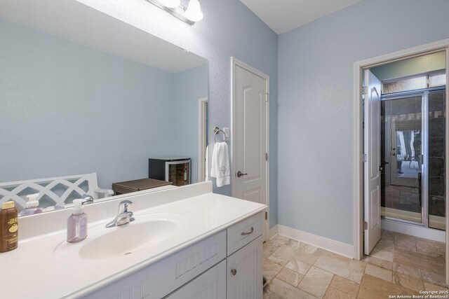 bathroom with stone tile floors, a stall shower, baseboards, and vanity