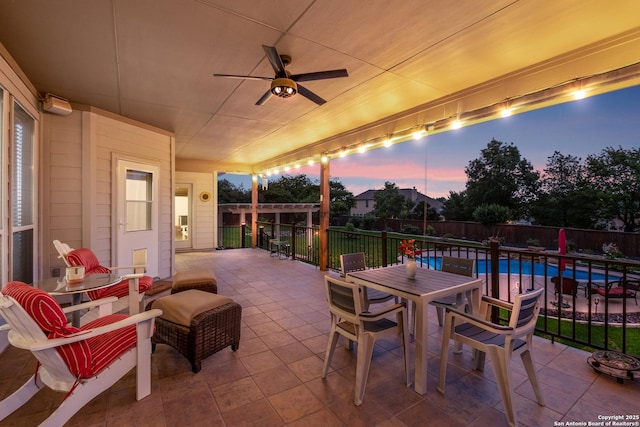 patio terrace at dusk with a fenced in pool, a ceiling fan, a fenced backyard, and outdoor dining space