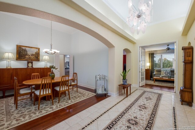 tiled dining room with crown molding, a high ceiling, an inviting chandelier, arched walkways, and baseboards