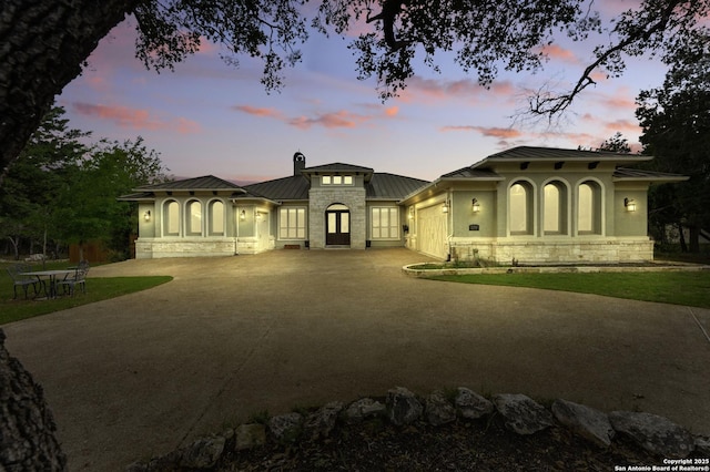mediterranean / spanish-style house featuring a garage, stone siding, a standing seam roof, metal roof, and driveway