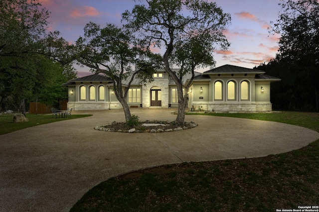 back of house featuring a standing seam roof, metal roof, curved driveway, stone siding, and stucco siding