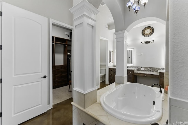 bathroom with a walk in closet, vanity, toilet, a whirlpool tub, and decorative columns