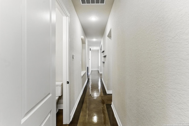 hall featuring visible vents, a textured wall, baseboards, recessed lighting, and concrete floors