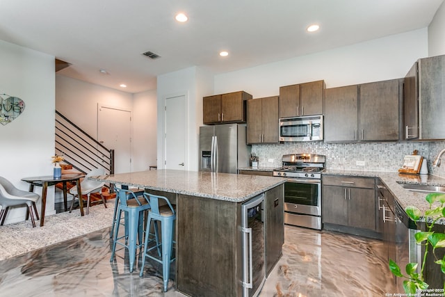 kitchen with dark brown cabinetry, a sink, stainless steel appliances, backsplash, and a kitchen island