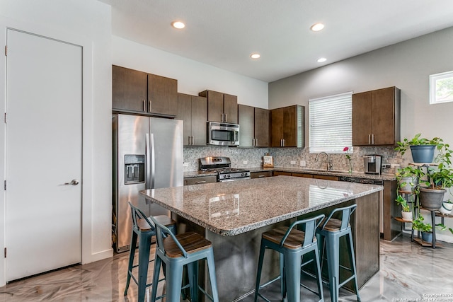 kitchen featuring appliances with stainless steel finishes, a sink, a kitchen breakfast bar, marble finish floor, and a kitchen island