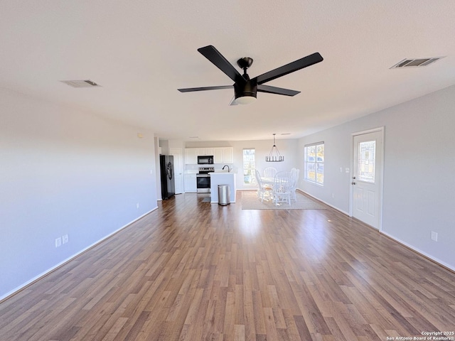 726 Barbara Dr, Canyon Lake, TX 78133 - unfurnished living room featuring visible vents, ceiling fan with notable chandelier, and dark wood-type flooring