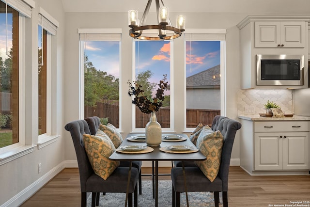dining space with baseboards, light wood finished floors, and a notable chandelier