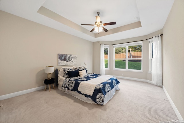 carpeted bedroom with baseboards, ceiling fan, and a tray ceiling