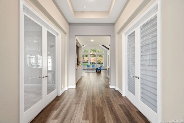 hallway with a tray ceiling, baseboards, french doors, and wood finished floors