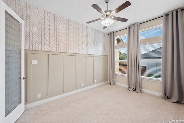 spare room with a wainscoted wall, ceiling fan, wallpapered walls, and carpet floors