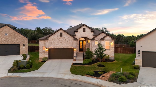 french country home with fence, a yard, stone siding, and concrete driveway