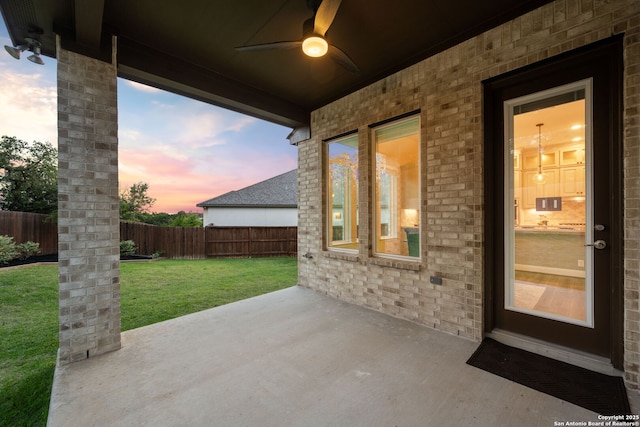 patio terrace at dusk with a yard, a ceiling fan, and a fenced backyard