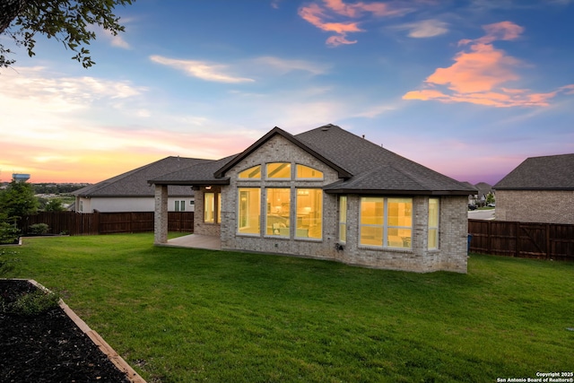 back of property at dusk with a shingled roof, a yard, and brick siding