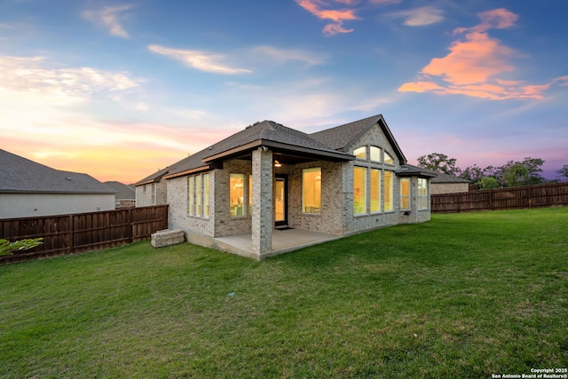 back of house at dusk with a fenced backyard, a patio, a lawn, and brick siding