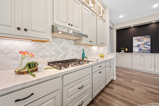 kitchen featuring glass insert cabinets, light wood-style floors, white cabinetry, under cabinet range hood, and stainless steel gas stovetop