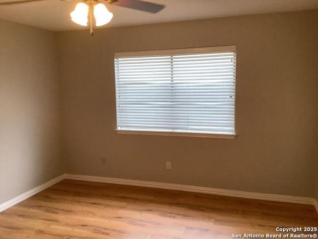 spare room featuring light wood-style floors, baseboards, ceiling fan, and a wealth of natural light