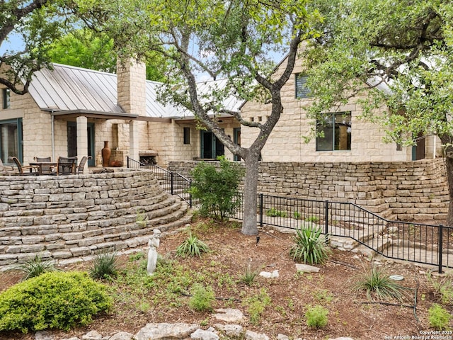 back of property featuring a standing seam roof, a chimney, fence, stairs, and stone siding