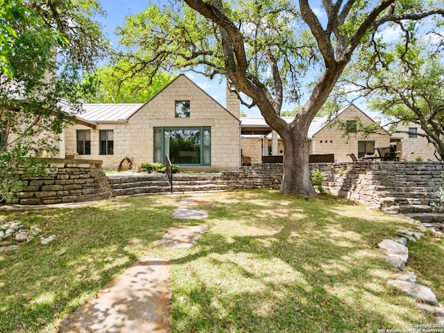 rear view of house featuring metal roof, a yard, a chimney, and a standing seam roof