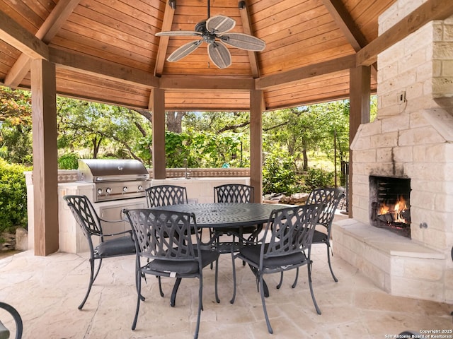 view of patio with ceiling fan, outdoor dining area, an outdoor stone fireplace, a gazebo, and a grill