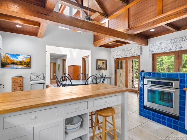 kitchen with a breakfast bar area, beam ceiling, wood counters, light tile patterned flooring, and oven