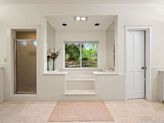 bathroom featuring tile patterned flooring, a bath, a stall shower, and tile walls