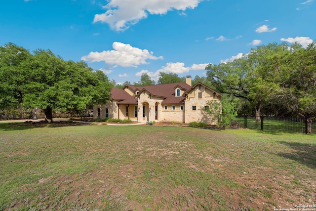 view of front facade featuring fence, a chimney, stone siding, and a front lawn