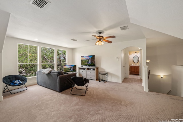 living area featuring visible vents, arched walkways, ceiling fan, and light colored carpet