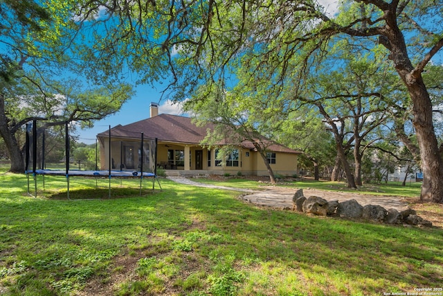 back of property with a yard, a chimney, and a trampoline