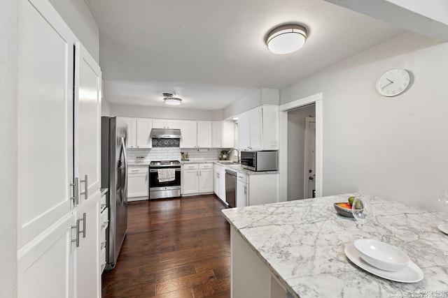 kitchen with dark wood-style floors, under cabinet range hood, white cabinets, tasteful backsplash, and appliances with stainless steel finishes