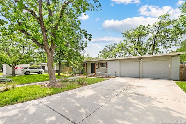 single story home featuring fence, a front yard, brick siding, an attached garage, and driveway