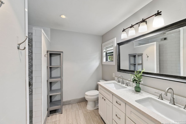 bathroom featuring double vanity, a sink, toilet, and tiled shower