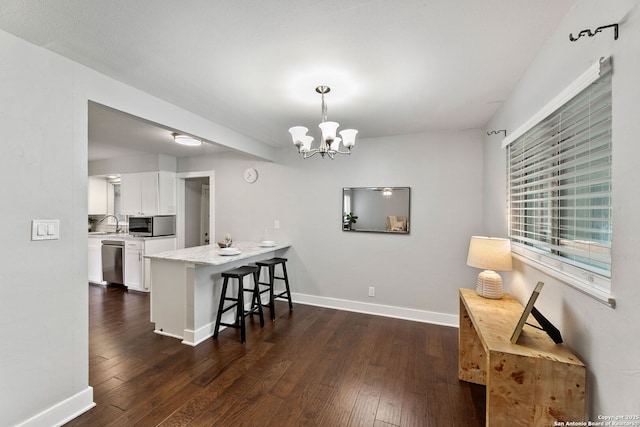 kitchen featuring white cabinets, appliances with stainless steel finishes, a breakfast bar area, a chandelier, and dark wood-style floors