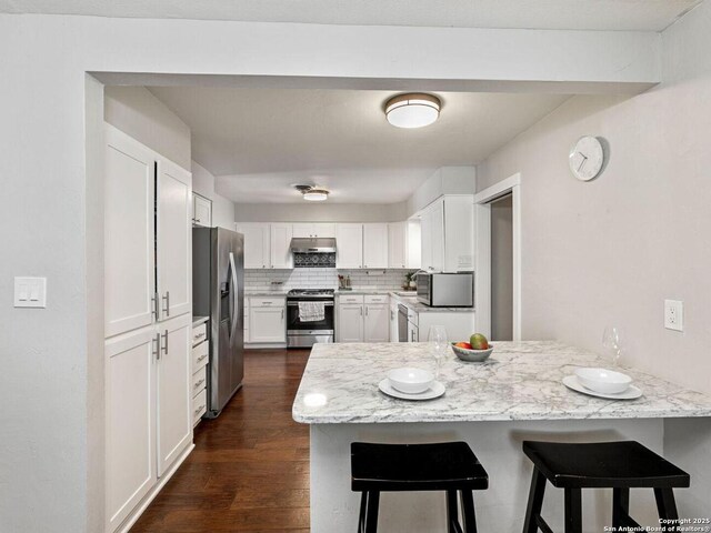 kitchen featuring a kitchen breakfast bar, stainless steel appliances, a peninsula, and under cabinet range hood