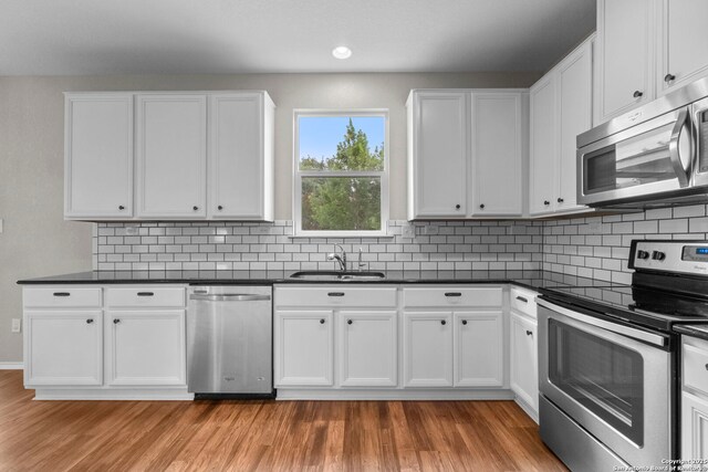 kitchen with stainless steel appliances, dark countertops, a sink, and light wood-type flooring