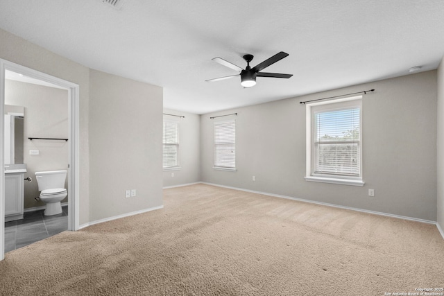 unfurnished bedroom with carpet flooring, baseboards, multiple windows, and ensuite bathroom