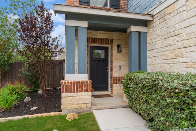 view of exterior entry with covered porch, brick siding, fence, and stone siding