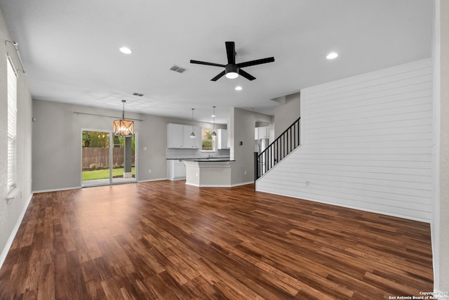 unfurnished living room featuring dark wood-style flooring, ceiling fan with notable chandelier, stairs, recessed lighting, and visible vents
