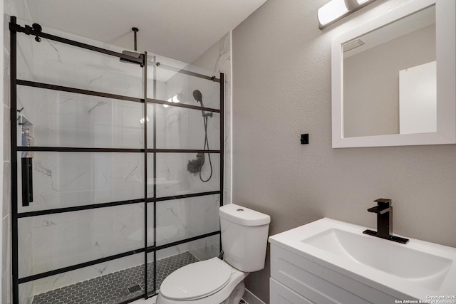 bathroom with toilet, a textured wall, a marble finish shower, and vanity