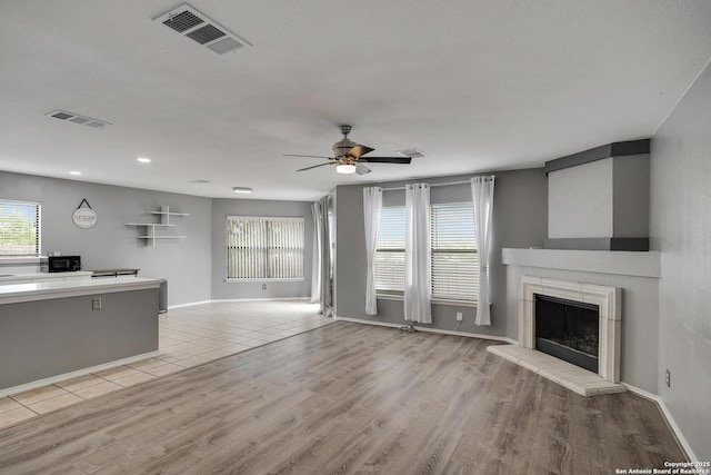 unfurnished living room with visible vents, a ceiling fan, a fireplace with raised hearth, and light wood-type flooring