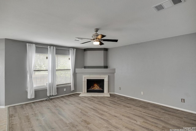 unfurnished living room featuring visible vents, wood finished floors, baseboards, ceiling fan, and a warm lit fireplace
