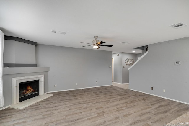 unfurnished living room featuring visible vents, ceiling fan, wood finished floors, and a warm lit fireplace