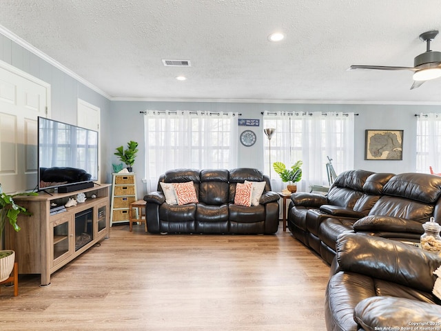 living room with crown molding, a textured ceiling, visible vents, and light wood-type flooring
