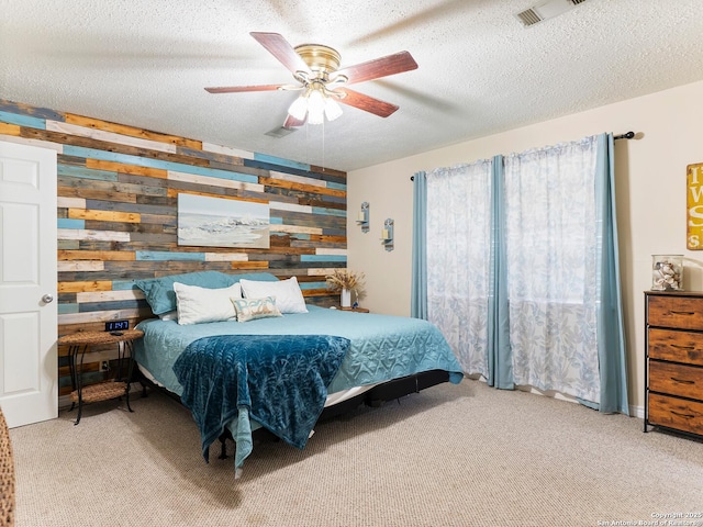 carpeted bedroom featuring visible vents, wood walls, a textured ceiling, and a ceiling fan