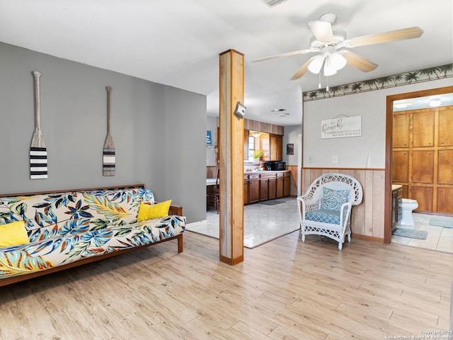 living area with ceiling fan, a wainscoted wall, and light wood-style floors