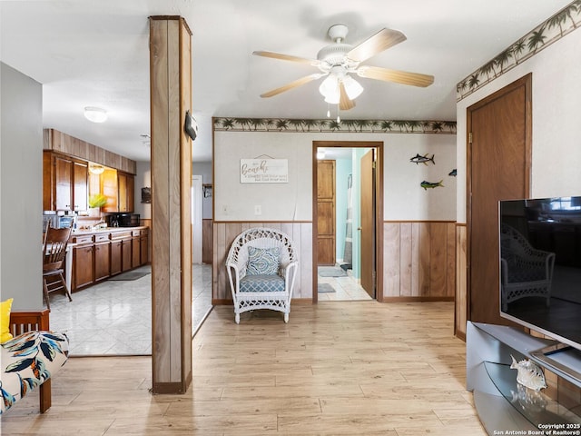 living area with wood walls, ceiling fan, wainscoting, and light wood-type flooring