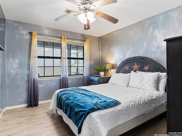bedroom with ceiling fan, visible vents, wood finished floors, baseboards, and a textured wall