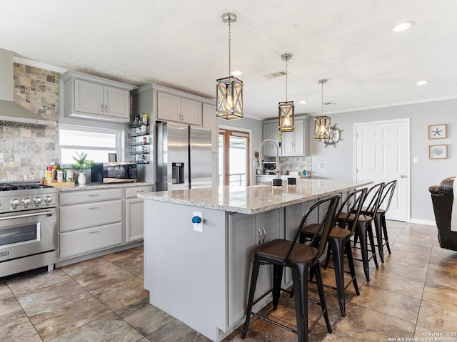 kitchen featuring wall chimney range hood, gray cabinets, stainless steel appliances, backsplash, and ornamental molding